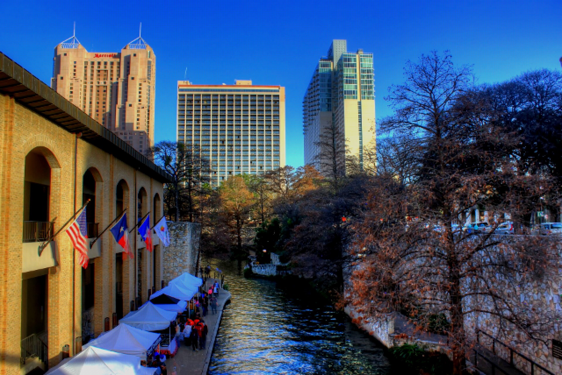 The San Antonio River Walk on a sunny day, with downtown towers behind the trees